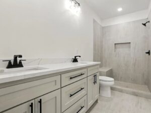 Modern bathroom with a double sink vanity, black fixtures, white countertops, light-colored cabinetry, a walk-in shower with built-in bench and niche, and neutral-toned tile flooring and walls.